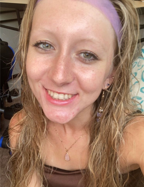 Emily smiling in a selfie. She has long dark blonde hair and is wearing a brown tanktop and purple headband