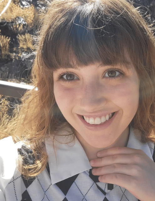 Photo of Jade smiling. Shes wearing a white collared shirt and has brownish hair with bangs